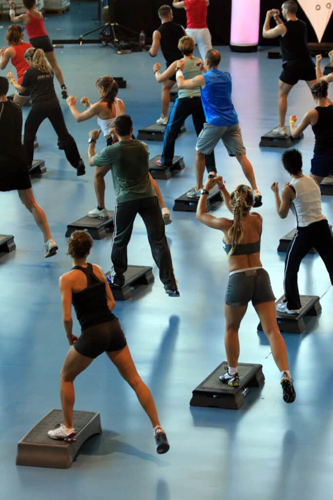 Cours de fitness dynamique avec un groupe de personnes en sportswear faisant du step aérobic et des mouvements de boxe sur des plateformes bleues.